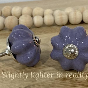 May include: Two purple ceramic cabinet knobs with a starburst design and a silver metal base. The knobs have a textured finish and are slightly lighter in colour than they appear in the image.