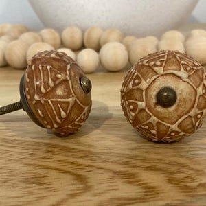 May include: Two ceramic cabinet knobs with a brown and white geometric design. The knobs have a brass screw and are perfect for adding a touch of rustic charm to any home.