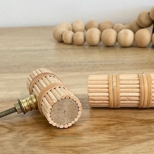 May include: Two wooden cabinet knobs with a natural wood finish and a brass screw. The knobs are made of thin strips of wood that are stacked and glued together. The knobs are approximately 5 cm in length.