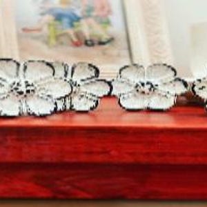 May include: Five white ceramic drawer pulls with a floral design. The pulls have a black outline and are arranged in a row on a red surface.