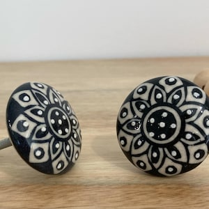 May include: Two black and white ceramic drawer knobs with a mandala design. The knobs have a white centre with black dots and a black outer ring with white details.