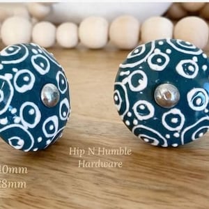 May include: Two teal blue ceramic knobs with a white swirl pattern. The knobs have a silver metal base. The text "Hip N Humble Hardware" is visible below the knobs.