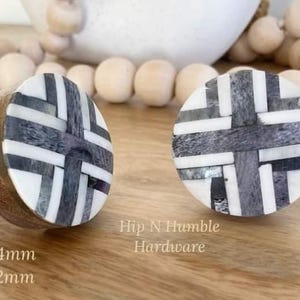 May include: Two decorative cabinet knobs with a geometric design in black, white, and grey. The knobs are round with a wooden base and a metal screw. The text "Hip N Humble Hardware" is visible.