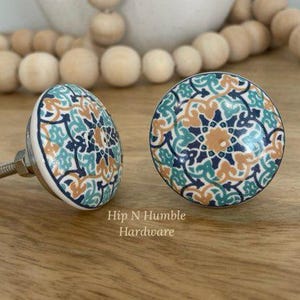 May include: Two ceramic cabinet knobs with a blue, green and orange geometric pattern. The knobs have a silver metal screw.