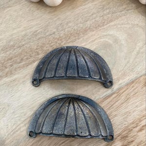 May include: Two antique-style cabinet pulls with a scalloped design. The pulls are made of metal and have a dark bronze finish.