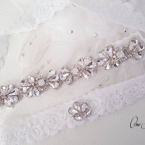 May include: White lace garter with a silver rhinestone embellishment. The garter has a small, separate rhinestone piece attached to it. The text "One Fancy Day" is visible in the bottom right corner of the image.