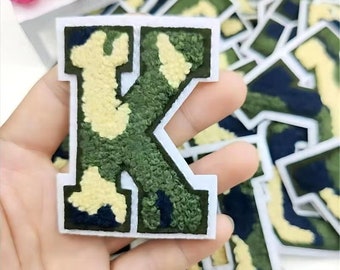 May include: A green, yellow, and black camouflage fabric letter K patch with white stitching. The patch is iron-on and can be used to personalize clothing, bags, and other items.