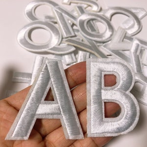 Może przedstawiać: Białe filcowe litery A i B z białym obramowaniem. Litery znajdują się na białym tle.