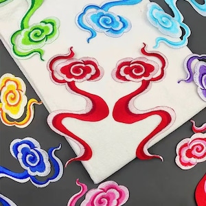 May include: Assortment of colourful embroidered iron-on patches featuring swirling cloud designs. The patches are in shades of green, blue, red, pink, yellow, and purple.