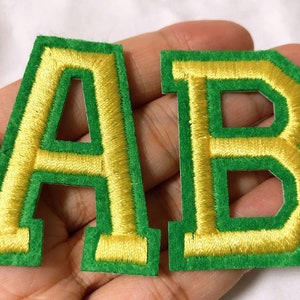 May include: Two felt letters, A and B, with a green background and yellow stitching. The letters are in a blocky, uppercase font.