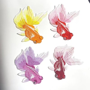 May include: Four embroidered iron-on patches of goldfish in different colours: yellow, pink, purple, and red. The goldfish are all facing the same direction with their tails fanned out.