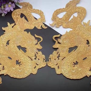 Puede incluir: Dos parches de hierro bordados en oro con un diseño de dragón. Los dragones están enroscados con sus colas en sus bocas.
