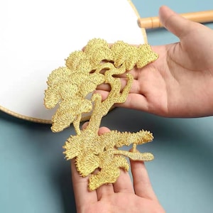 May include: Gold embroidered patch depicting a stylised tree with intricate details. The patch is ideal for adding a touch of elegance to clothing, bags, or home decor.