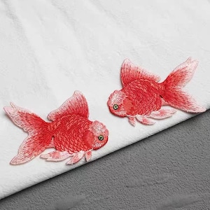 May include: Two red embroidered goldfish patches. The patches are on a white fabric background. The text "金鱼*刺绣" is in the lower right corner of the image.