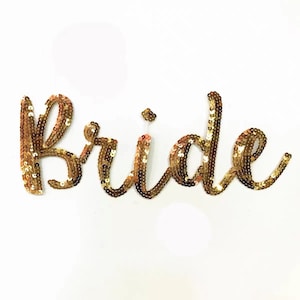 May include: Gold sequined "bride" patch. The patch is made of gold sequins and is shaped like the word "bride".