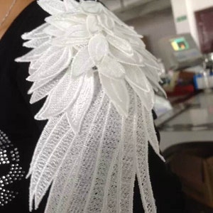 Può includere: Una camicia nera con un'applicazione in pizzo bianco a forma di ala sulla spalla.