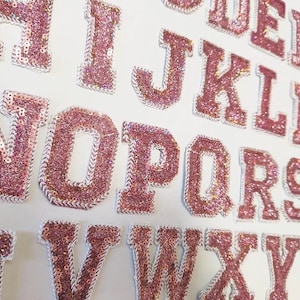Op de afbeelding: Roze glitter alfabetletters met witte contouren. Elke letter is individueel gestikt en heeft een glinsterende afwerking.