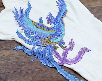 Puede incluir: Una aplicación bordada de un fénix azul y dorado con plumas moradas. El fénix es un ave mítica que simboliza el renacimiento y la inmortalidad.