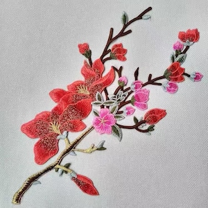 May include: A delicate embroidered patch featuring a floral design with pink and red flowers. The flowers are arranged on a branch with green leaves. The patch is perfect for adding a touch of elegance to clothing, bags, or other crafts.