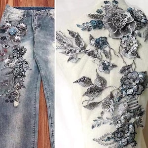 Puede incluir: Una aplicación floral plateada y azul con lentejuelas y cuentas. La aplicación está sobre un fondo de malla blanca.