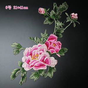 May include: Pink and white embroidered flower applique with green leaves. The applique measures 21 by 41 centimeters.
