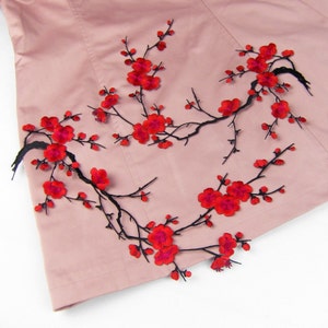 May include: A pink fabric with black embroidered branches and red flowers. The flowers are in the shape of cherry blossoms.