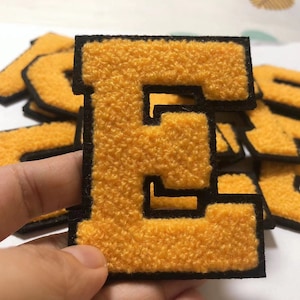 Könnte beinhalten: Nahaufnahme eines gelben Filzbuchstabens E mit schwarzen Nähten. Der Buchstabe ist von anderen gelben Filzbuchstaben umgeben.