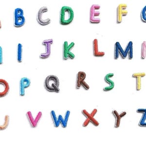 May include: A collection of twenty-six individual embroidered alphabet letter patches arranged in rows. Each letter features a distinct thread color, including orange, blue, silver, green, pink, yellow, purple, red, brown, and light blue, with a white border.