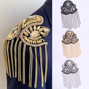 May include: Three gold, silver, and black jeweled shoulder patches with dangling chains. Each patch features a decorative design with rhinestones and beads.