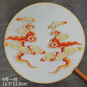 Può includere: Due toppe ricamate con un design a nuvola stilizzato in tonalità arancio, rosso e oro. Le toppe misurano 12,5 pollici per 13,5 pollici e sono esposte su uno sfondo bianco.