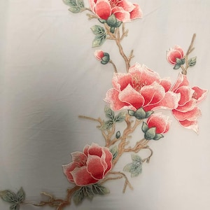 Op de afbeelding: Een delicaat bloemenborduurmotief met roze bloemen en groene bladeren op een witte achtergrond. De borduurwerk is perfect om kleding, woonaccessoires of knutselprojecten een vleugje elegantie te geven.