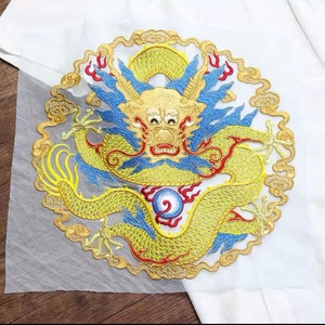 Könnte beinhalten: Ein goldfarbener gestickter Aufnäher mit einem detaillierten Drachen mit blauen und roten Akzenten. Der Drache ist von Wolken und einer Perle umgeben.