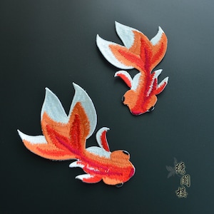 Könnte beinhalten: Zwei gestickte Bügelbilder von orangefarbenen und weißen Goldfischen. Die Patches befinden sich auf einem schwarzen Hintergrund.