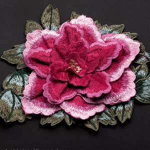 Puede incluir: Una gran flor bordada de color rosa y rojo con hojas verdes. La flor es una peonía, una flor popular por su belleza y simbolismo.
