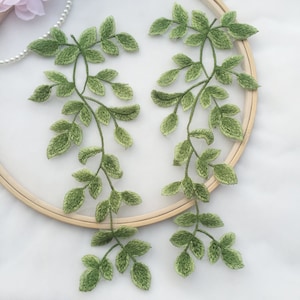 May include: Two green embroidered leafy vines with a light green colour gradient. The vines are displayed on a wooden embroidery hoop.