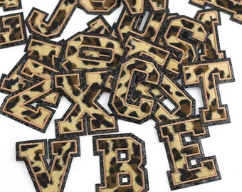 May include: A collection of leopard print iron-on patches in the shape of uppercase letters. The patches are brown and black with a fuzzy texture.