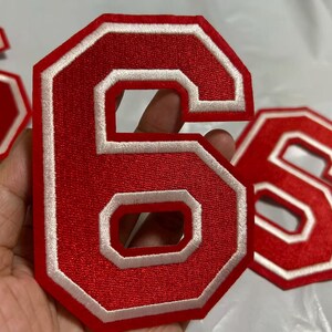 May include: Red embroidered number 6 patch with a white border. The number is in a bold, block style. Several patches are visible, suggesting a set or collection of numbers for customization.
