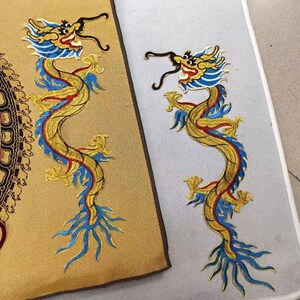 May include: Two embroidered dragon patches featuring a serpentine body in gold, blue, and red thread. One dragon is applied to a textured gold fabric, while the other is placed on a light grey surface. Both dragons have long whiskers.