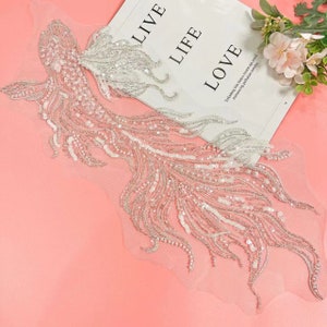 May include: A white beaded and sequined applique in the shape of a feather, with a delicate tulle backing.