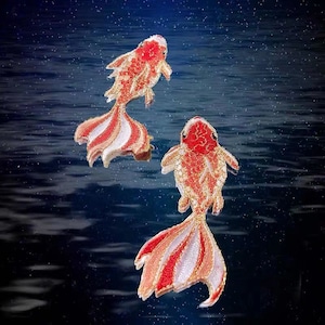 Könnte beinhalten: Zwei gestickte Goldfische mit roten und weißen Schuppen, die vor einem dunkelblauen Hintergrund mit weißen Punkten schwimmen.