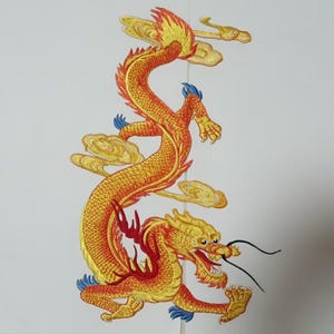 Peut inclure: Broderie d'un dragon aux couleurs or, orange et rouge, avec des touches de bleu. Le dragon, au corps sinueux, est entouré de nuages stylisés. L'œuvre est réalisée sur fond blanc.