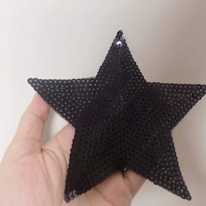 May include: A black star-shaped patch made of sequins. The patch is approximately 12.5 cm wide and 12.5 cm tall.