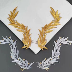 May include: Two sets of gold and silver leaf embroidery patches. The gold patches are in the shape of a wreath with leaves and small beads. The silver patches are in the shape of a half-circle with leaves and small beads.
