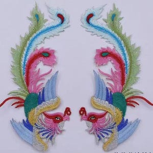 May include: Two embroidered iron-on patches featuring a colourful phoenix design with pink, blue, green and yellow accents. The phoenixes are facing each other with their wings spread out.