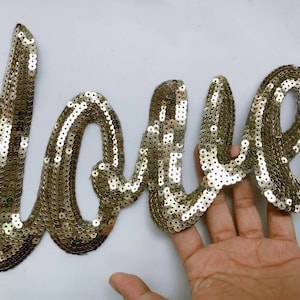 May include: Gold sequin applique in the shape of the word "love".
