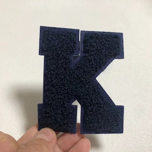 May include: A dark blue felt letter K, the letter is thick and fuzzy, the letter is cut out and has a white background.