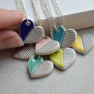 May include: A set of six ceramic heart necklaces with black and white stripes and a coloured half. The colours include blue, pink, teal, yellow, and purple.