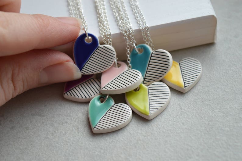 May include: A set of six ceramic heart necklaces with black and white stripes and a coloured half. The colours include blue, pink, teal, yellow, and purple.