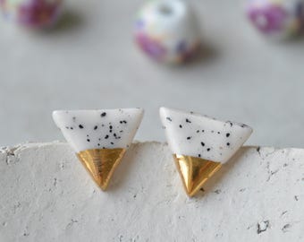 May include: A pair of white triangle shaped earrings with black speckles and gold trim.