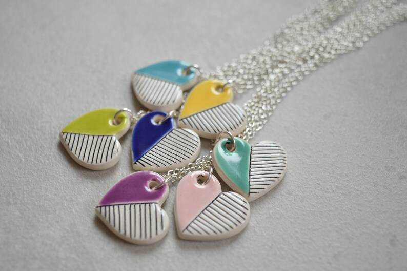 May include: A set of seven heart-shaped ceramic pendants with black and white stripes and different coloured accents. The pendants are attached to silver chains.